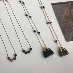 Makroansicht goldener Halsketten mit Anhängern aus Tigerauge und Obsidian Mini-Taschen