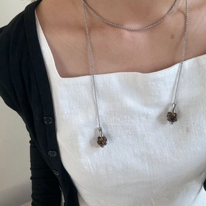 Silberne lange Kette mit braunen Steinkugeln, getragen über weißem Top und schwarzem Strick