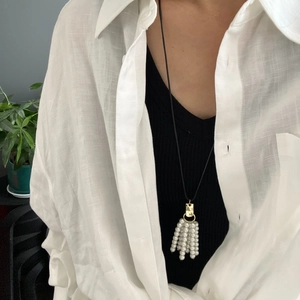 Detailweergave van een vergulde kwastjesketting met witte parels en lang zwart koord