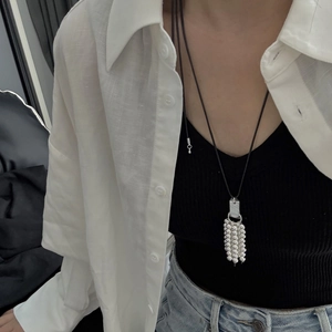 Detailopname van de zilveren kralenkwast aan een lange zwarte ketting gedragen door model