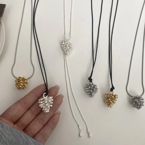 Detalle de collares con colgante de piña en oro y plata con cordones ajustables