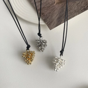 Detalle del collar con colgante de piña en acabados oro y plata con cordón negro