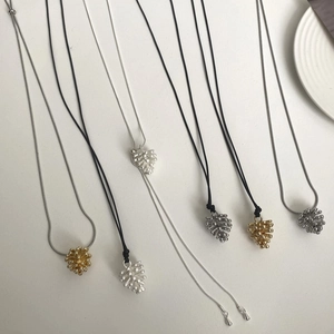 Detalle de los colgantes de piña en plata y oro con cordón negro y cadenas de metal