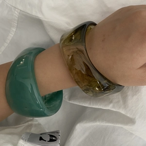 Close-up of stacked wide resin bangles in translucent emerald green and amber marble