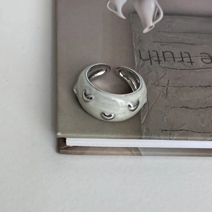 Close-up of light green enamel open ring with 3D silver heart charms on a book edge