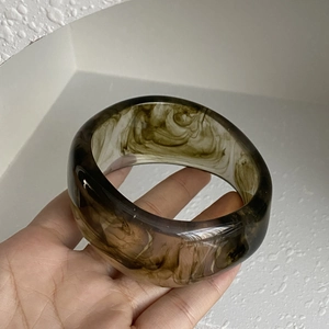 Macro shot of wide coffee-colored resin bangle with fluid ink-like sand texture