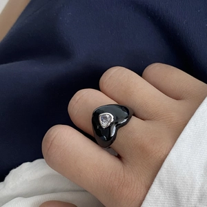 Close-up of black enamel heart ring with a heart-shaped zircon stone on a finger