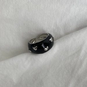 Detailed macro shot of adjustable black enamel ring with silver heart charms on white fabric