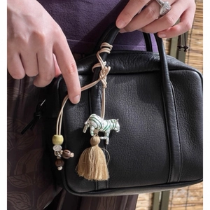 Ethnic style black leather handbag with zebra charm and tassel beads on bamboo background