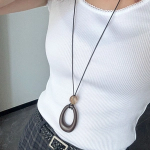 Detailed view of minimalist long brown pendant necklace on a model wearing white vest
