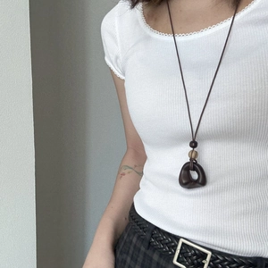 Close-up of bohemian brown resin pendant necklace with wooden beads on a white rib-knit top
