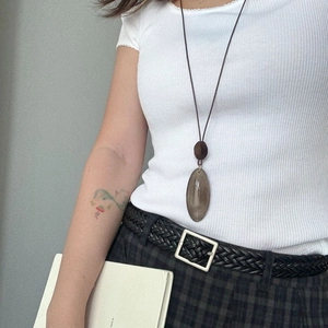 Close-up of translucent brown oval pendant on long leather cord shown on a model
