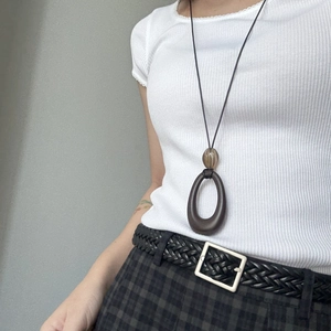Detail of a brown resin pendant necklace on a white ribbed T-shirt with woven belt