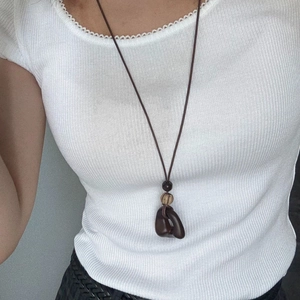 Detail of a brown Maillard tassel pendant necklace on a minimalist white ribbed sweater