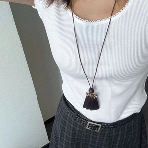 Detail of a brown tasseled long necklace on a white ribbed shirt for a minimalist look