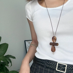 Detailed close-up of brown geometric resin pendant on a long necklace over white ribbed top