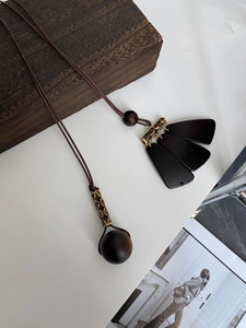 Detail of wooden fan-shaped pendants and textured bronze metal tubes on long necklace
