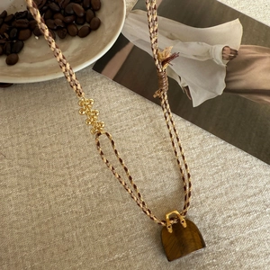 Detail view of tiger eye stone handbag pendant on a woven tassel sweater necklace