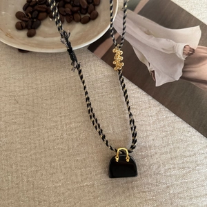 Detail of tiger eye bead tassel necklace featuring a black handbag-shaped pendant