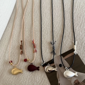 Detailed view of fish pendants in gold, silver, and burgundy on braided cords