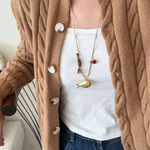 Close-up of golden fish pendant with red bead and tassel detail on a long beige cord