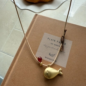 Detail of golden whale pendant with red bead on a thin woven cord necklace