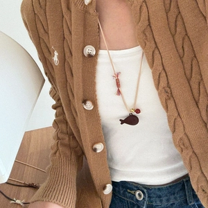 Detail of a fish pendant necklace styled with a brown knit cardigan and casual outfit