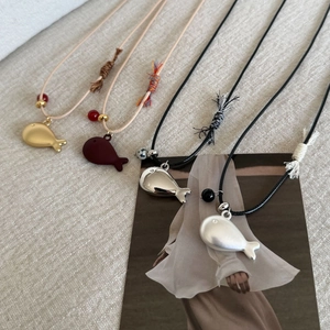 Macro detail of fish-shaped pendants in gold, silver and red on woven cord necklaces