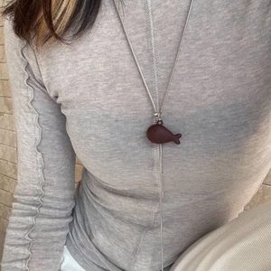 Detail of minimalist golden fish pendant with dark brown accents on long sleek chain