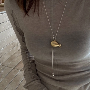 Detail view of a gold fish-shaped pendant on a long Y-shaped adjustable snake chain