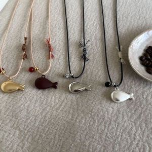 Detailed view of four colorful whale-shaped pendants on handcrafted woven necklaces