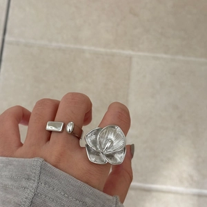 Detailed view of silver open geometric ring and textured 3D flower ring on hand