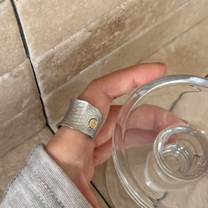 Detail of wide brushed silver ring with golden circle element worn on index finger