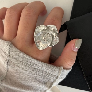 Macro view of a bold silver flower ring with intricate radial texture on a finger