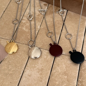 Oval pendant necklaces in gold, silver, red, and black finishes on a textured stone background