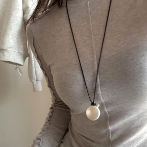 Detail view of minimalist oval pendant necklace on a textured grey long-sleeve shirt