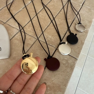 Detail view of five oval pendant necklaces in gold, silver, black, brown and white finishes