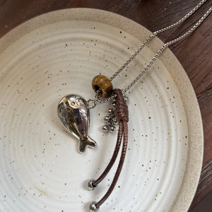Detail der Fisch-Halskette mit Tigerauge-Stein auf Keramikteller vor Holz Hintergrund