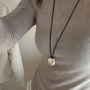 Long necklace with silver oval pendant and black leather cord worn over gray knitwear