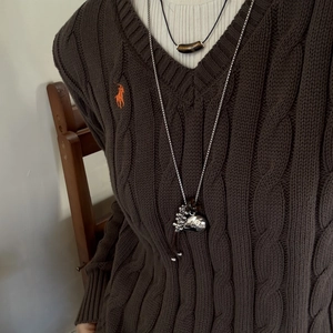 Detail eines dunkelbraunen Zopfstrickpullovers mit V-Ausschnitt und orangefarbenem Logo