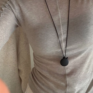 Detail view of the black matte oval pendant necklace worn on a grey knit sweater