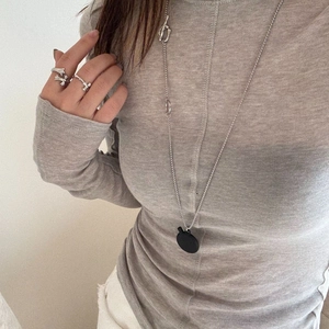 Detailed view of long necklace with oval pendant and silver carved rings on model