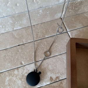 Detail of silver chain necklace with black matte circular pendant and T-bar clasp closure