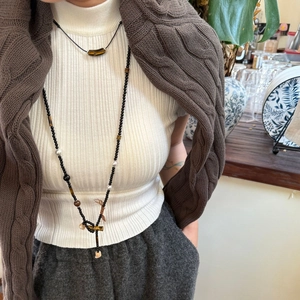 Detail einer langen Perlenkette mit Tigerauge-Steinen und Kreuzanhänger an einem Model