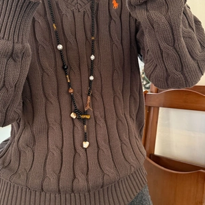 Detail der Perlenkette mit Tigerauge und Perlen auf braunem Strickpullover-Hintergrund