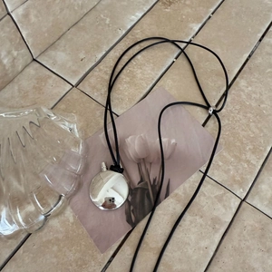 Detailed view of silver oval pendant with mirror finish and adjustable black leather cord