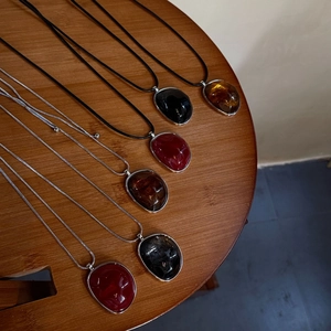 Detail view of resin pebble pendants in burgundy, black, and amber on a wooden table surface