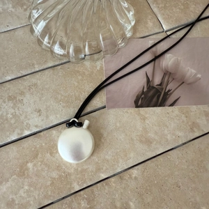 Detailed view of an elegant pearlescent oval bottle pendant on a minimalist black woven cord