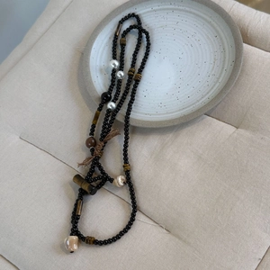 Detail einer langen Perlenkette mit schwarzem Achat, Tigerauge und brauner Quaste
