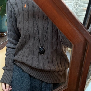 Close-up of resin oval pendant on black cord over brown sweater with wood mirror frame
